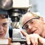 closeup picture: trainer and apprentice in vocational training on a milling machine - teacher explains details of the machine